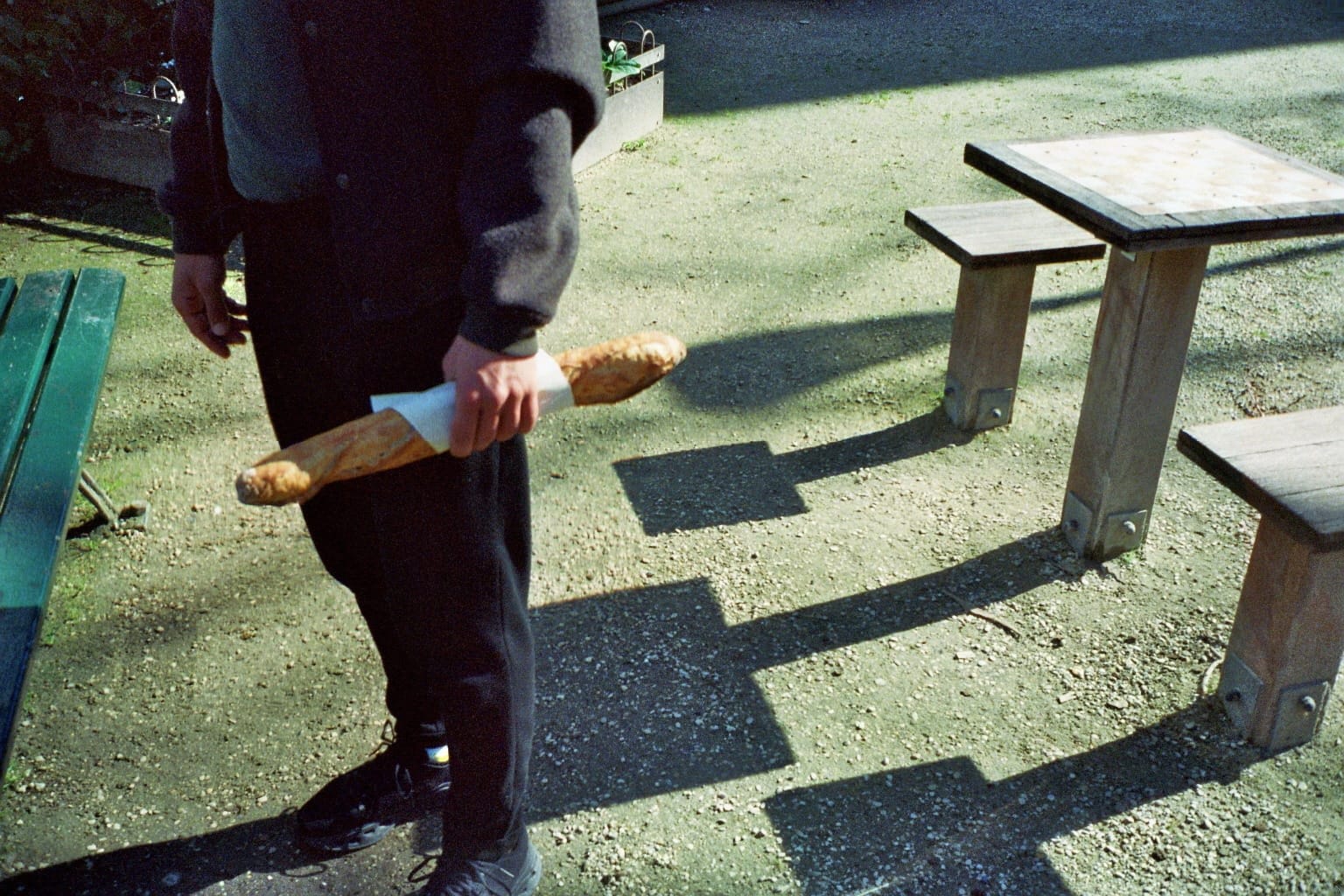 Film photo: someone holding a baguette next to a park bench