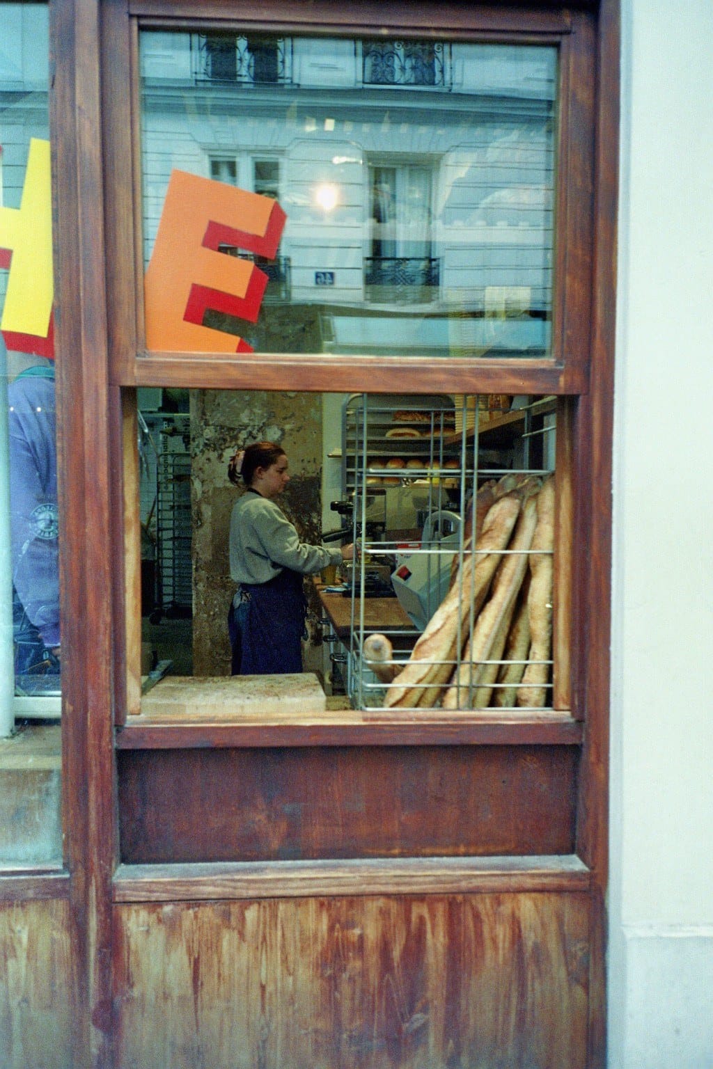 Film photo: a baker behind the window of a Paris bakery