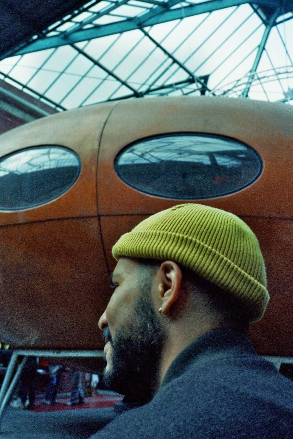 Film photo: a man in a yellow beanie in front of an orange capsule house