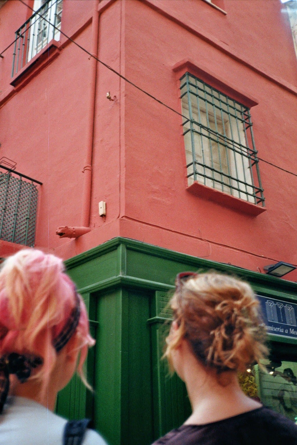 Film photo: two women looking up at a red house with a green shopfront