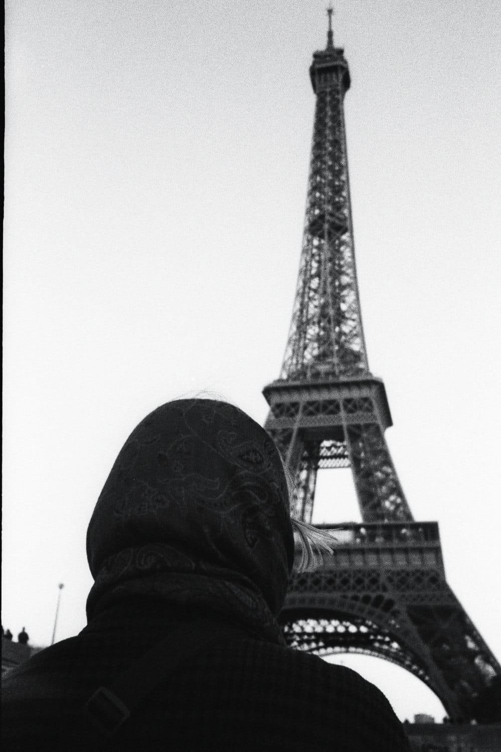 Black-and-white film photo: woman in a headscarf looking at the Eiffel Tower