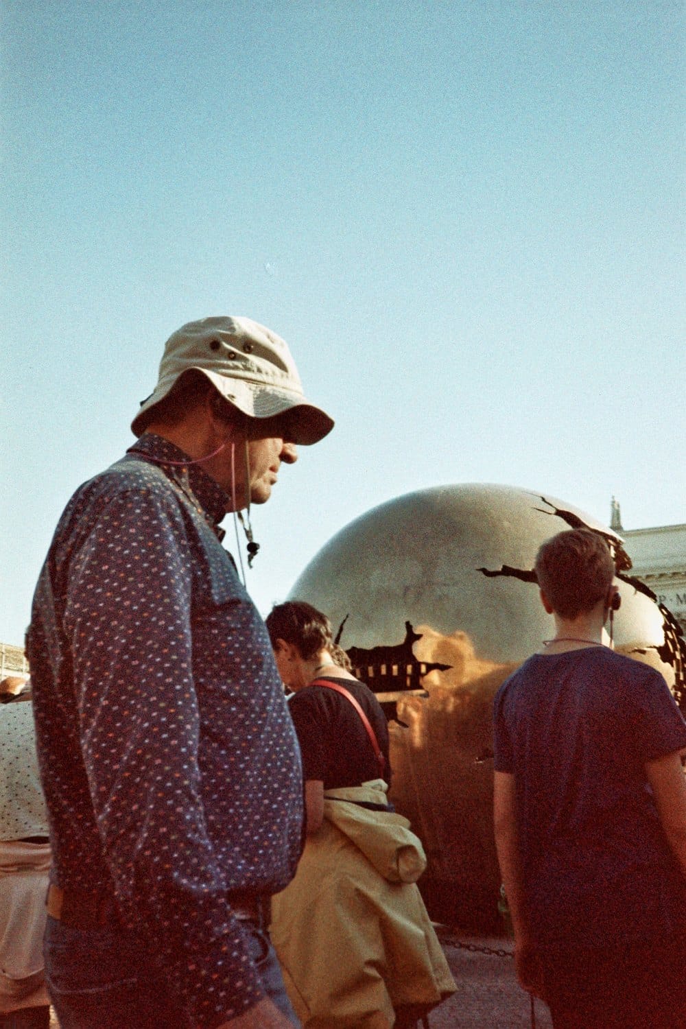 Film photo: man in a sun hat in front of a globe sculpture